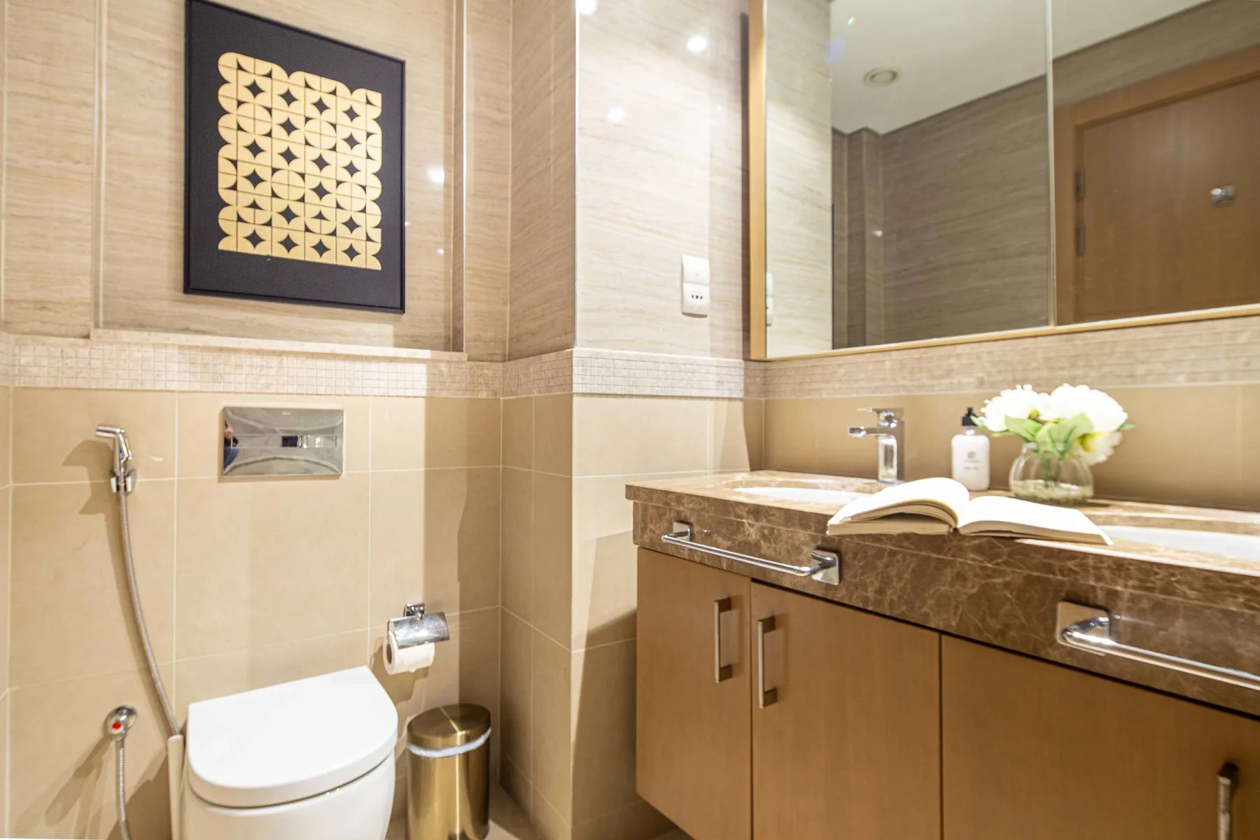 A bathroom with a toilet, wall-mounted shower, and a vanity beneath a large mirror.