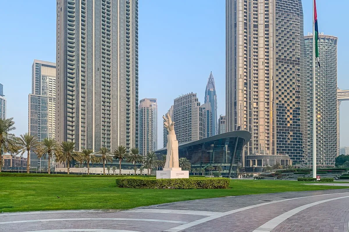 A landscaped plaza with a central statue, lawn, and surrounding high-rise buildings.