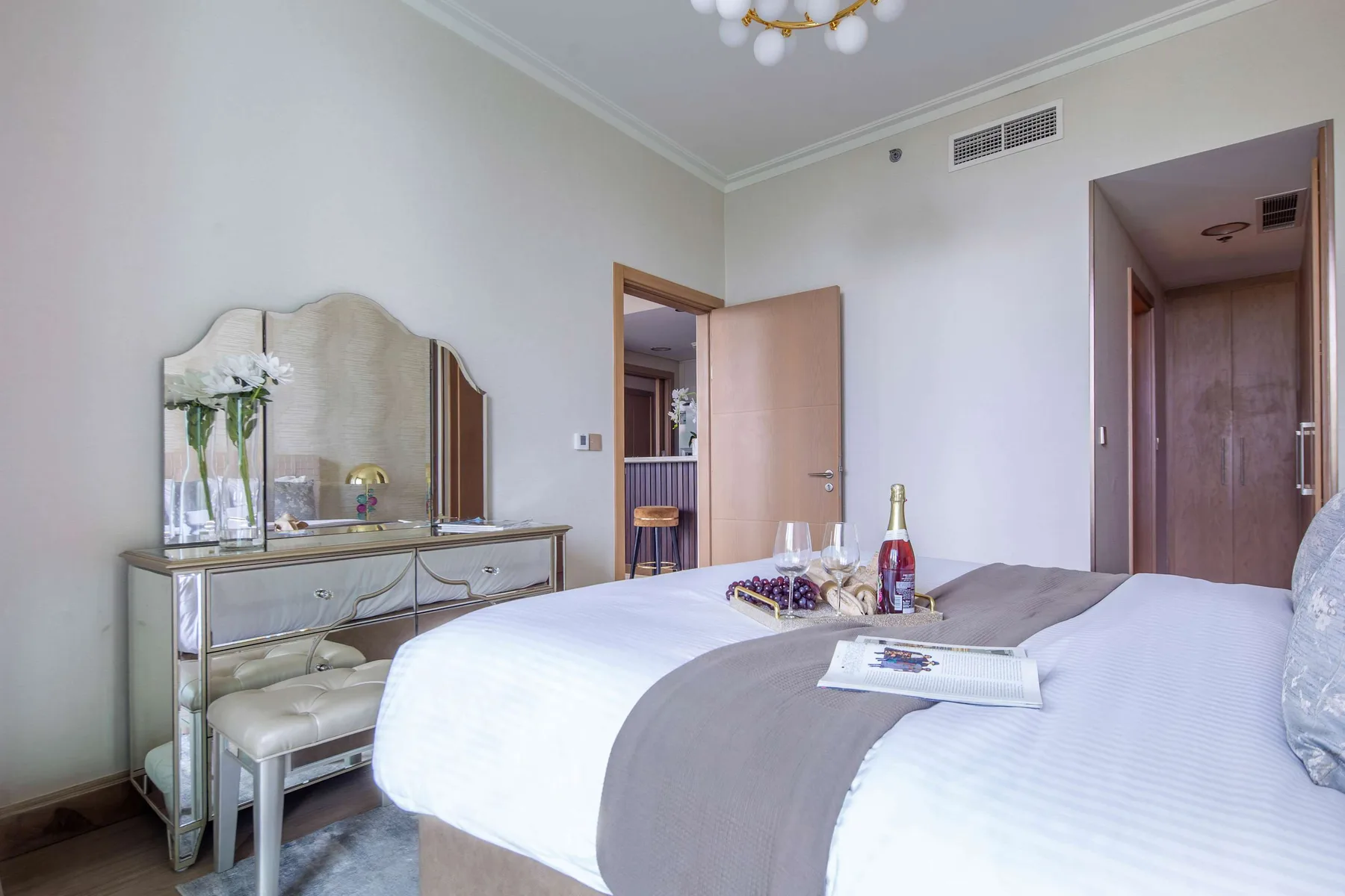 A bedroom with a neatly made bed and a mirrored dressing table.