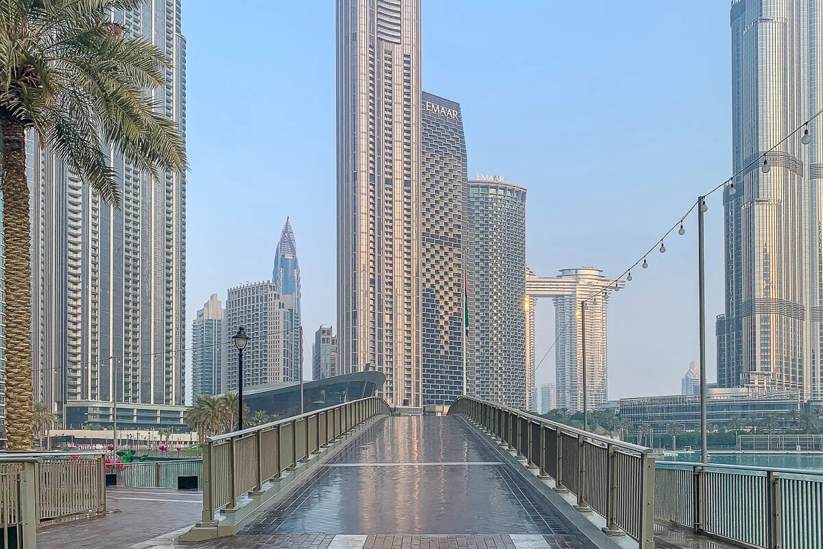 A pedestrian bridge extends toward a city skyline, with railings along the walkway.