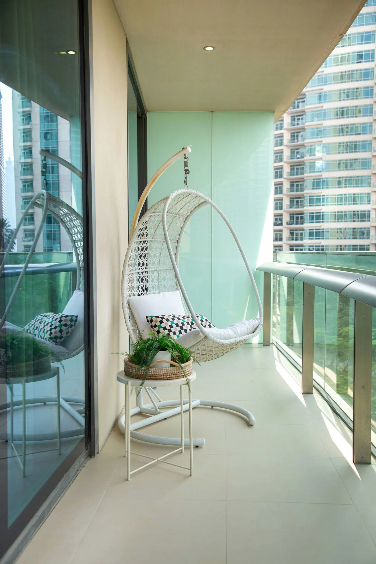 A balcony with a hanging chair and a small table beside the glass railing.