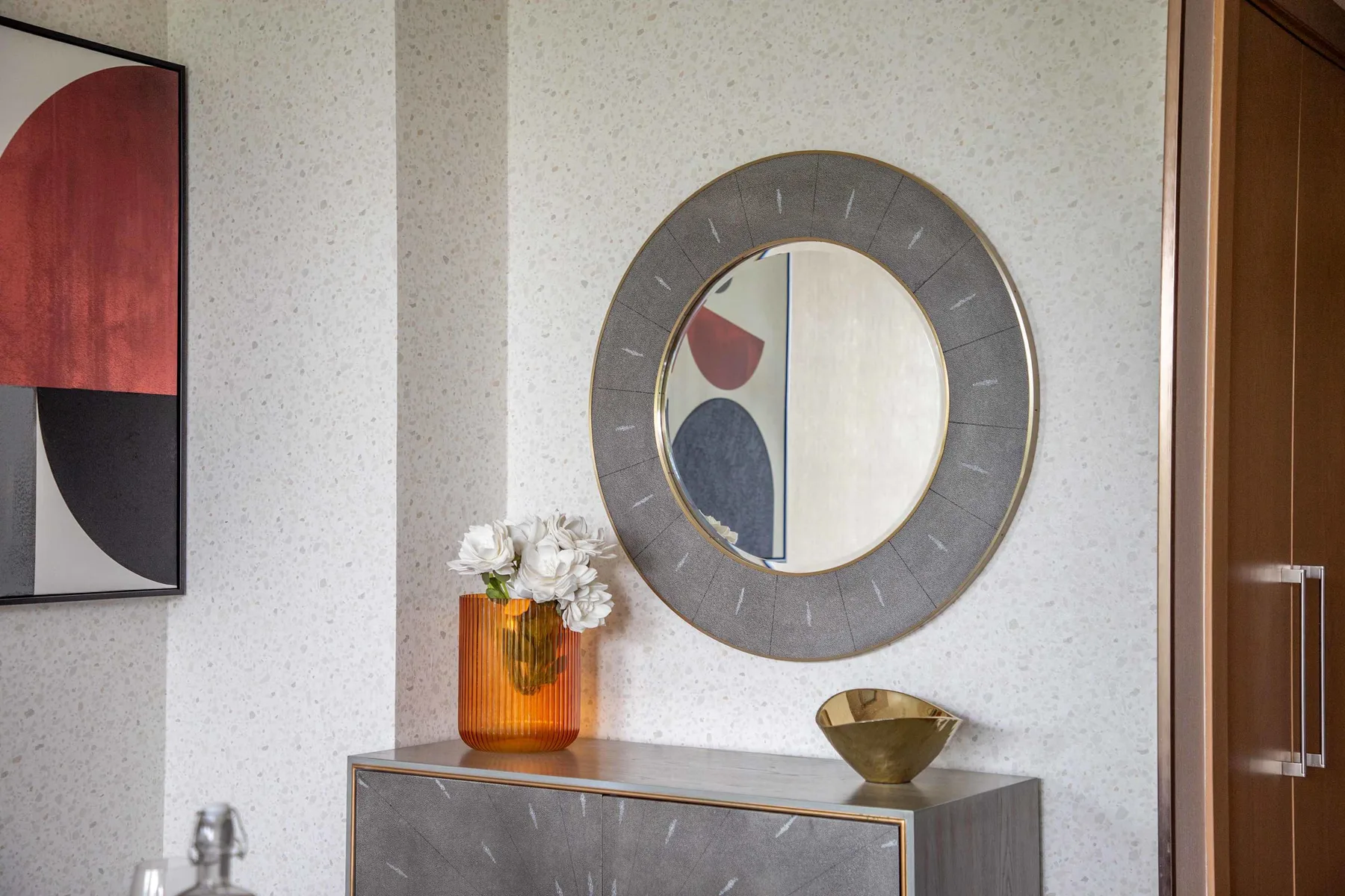 A decorated hallway wall features a round mirror above a console with flowers.