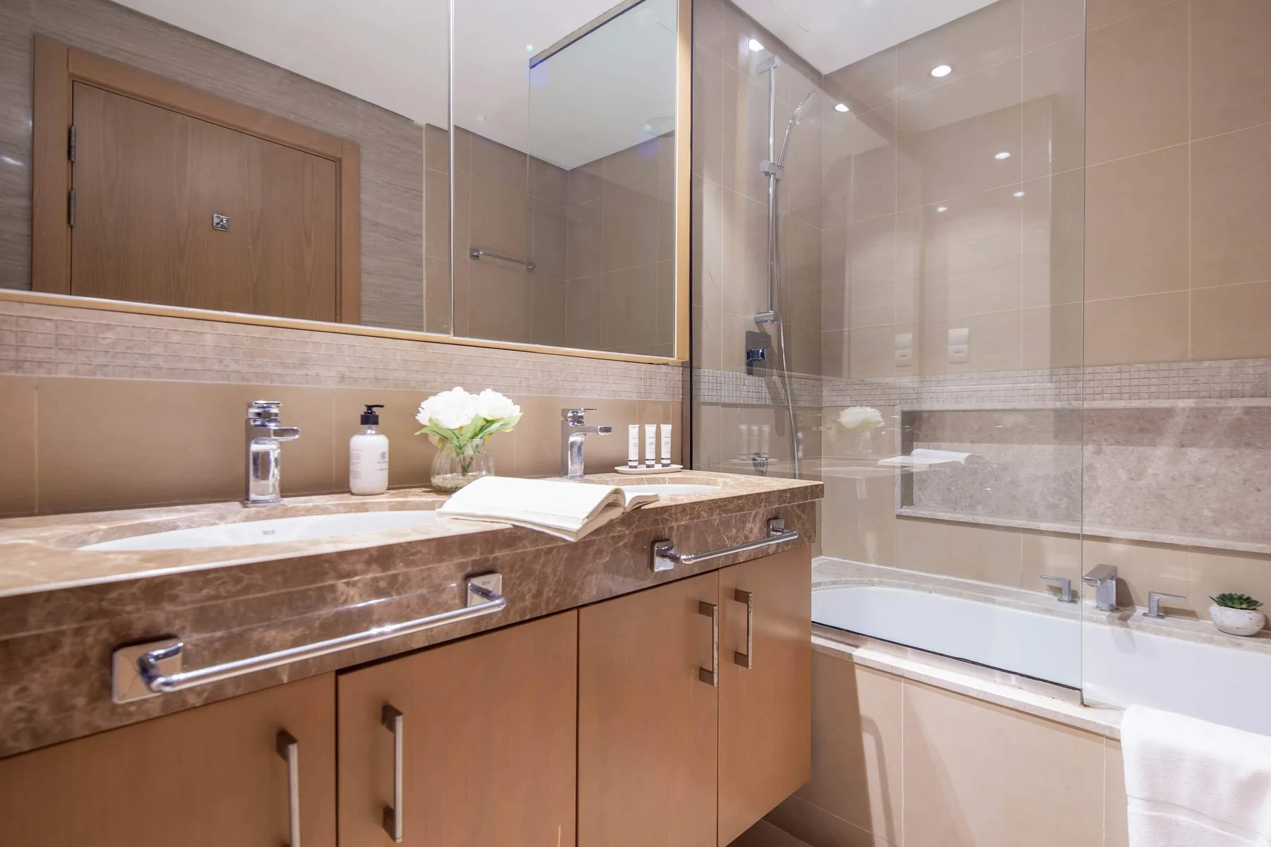 A bathroom with a long vanity and a bathtub behind a glass screen.