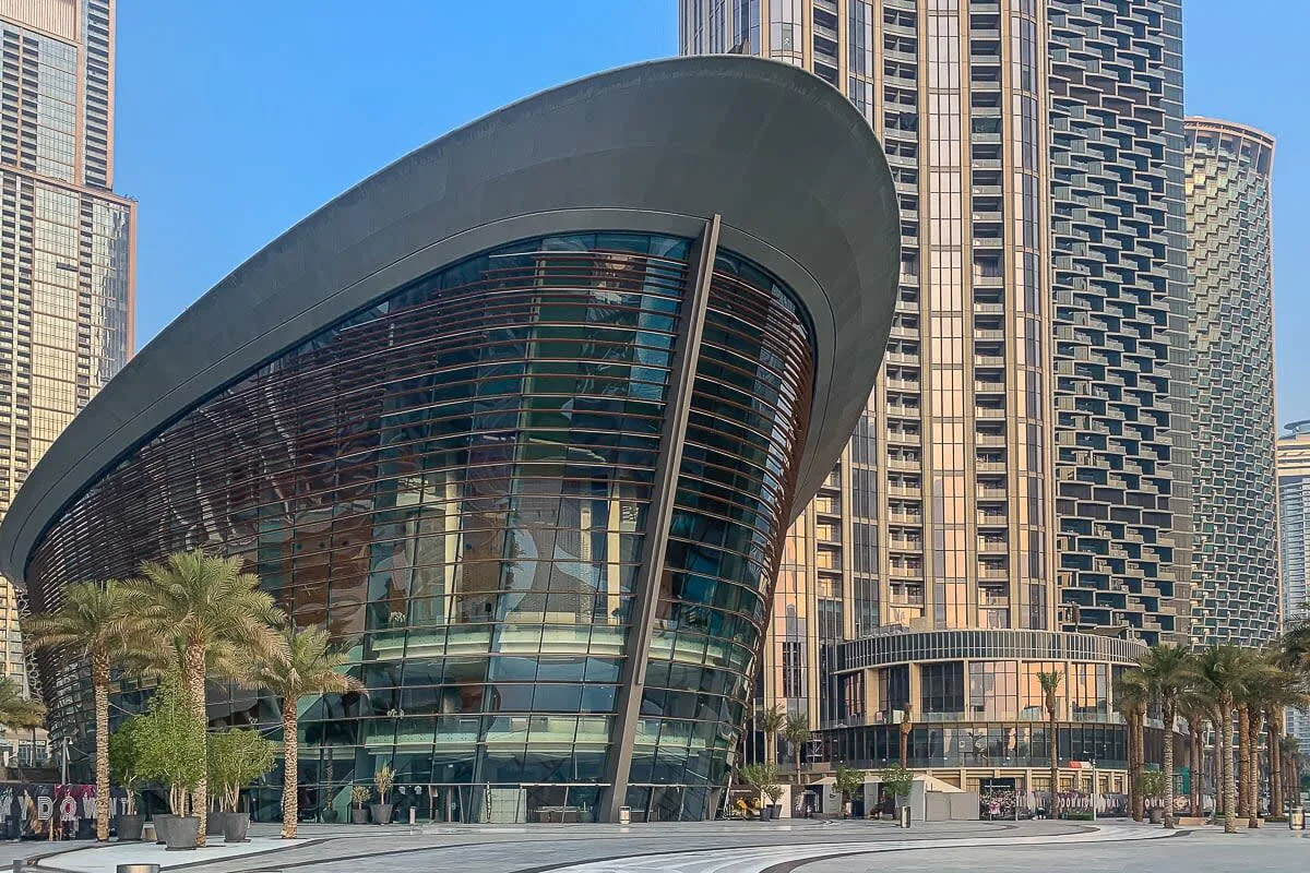 A curved glass-fronted building stands among tall towers along a palm-lined street.
