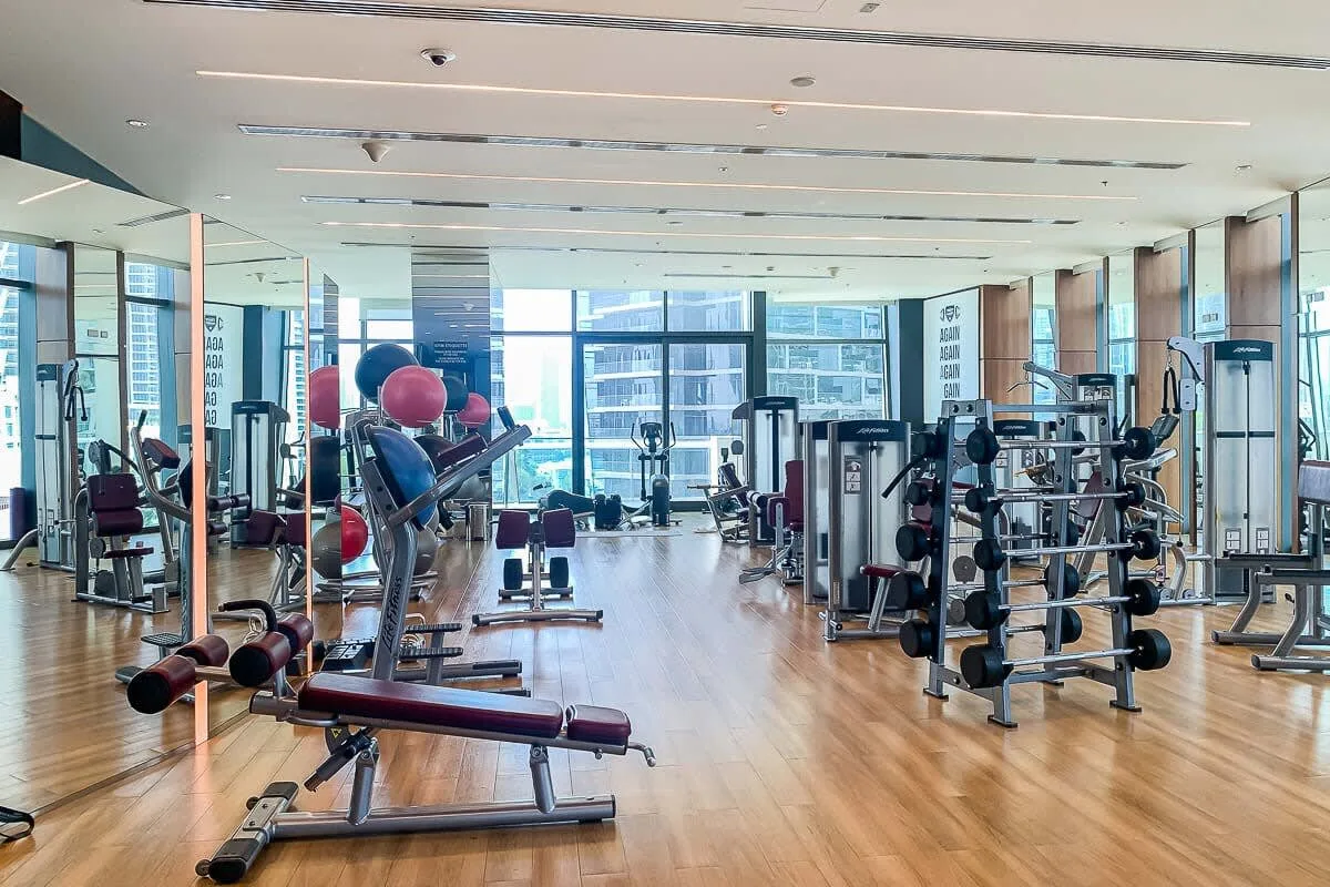 A spacious gym with exercise machines and weight benches beside large windows.