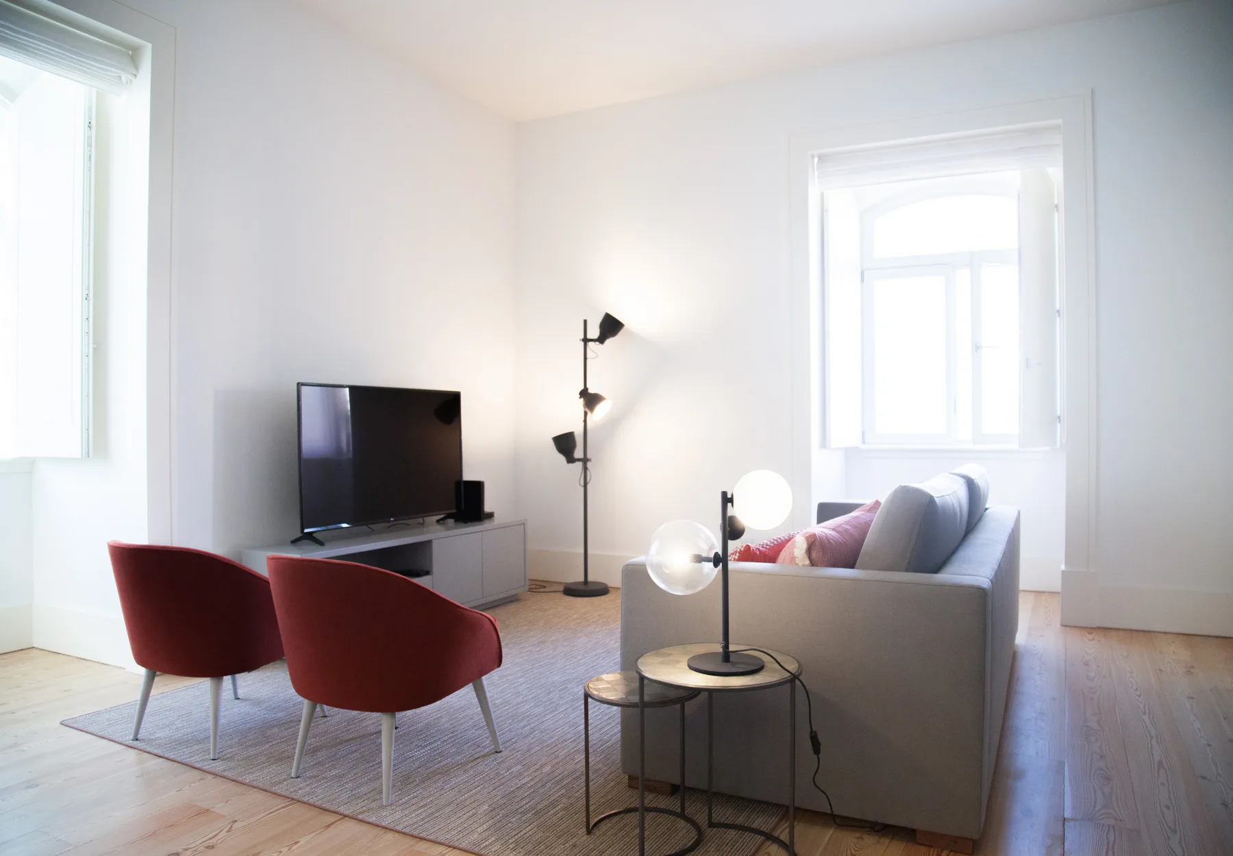 Una sala luminosa con un sofá, un televisor y dos asientos rojos.