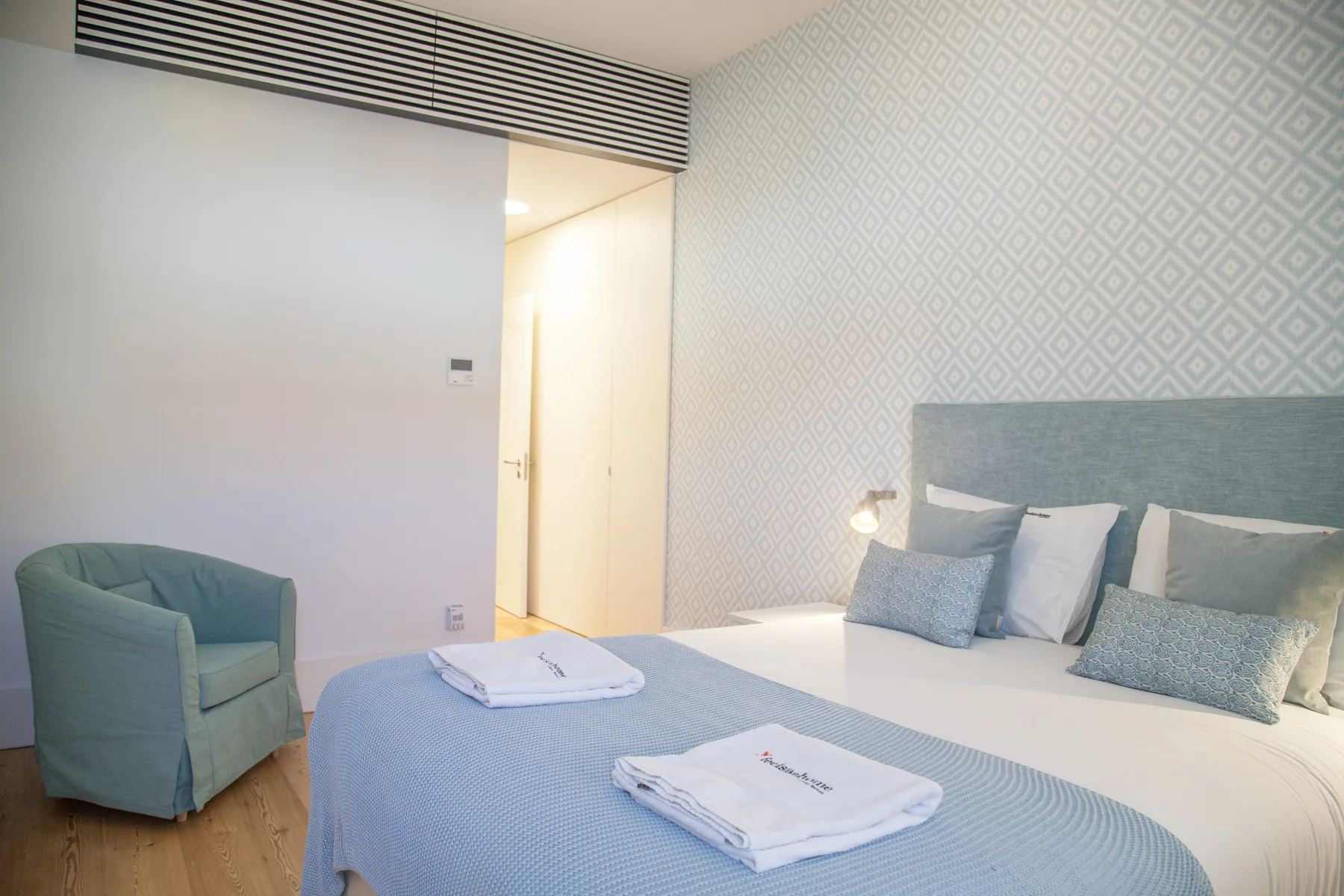 Un dormitorio con una cama, ropa de cama azul y un sillón acolchado.