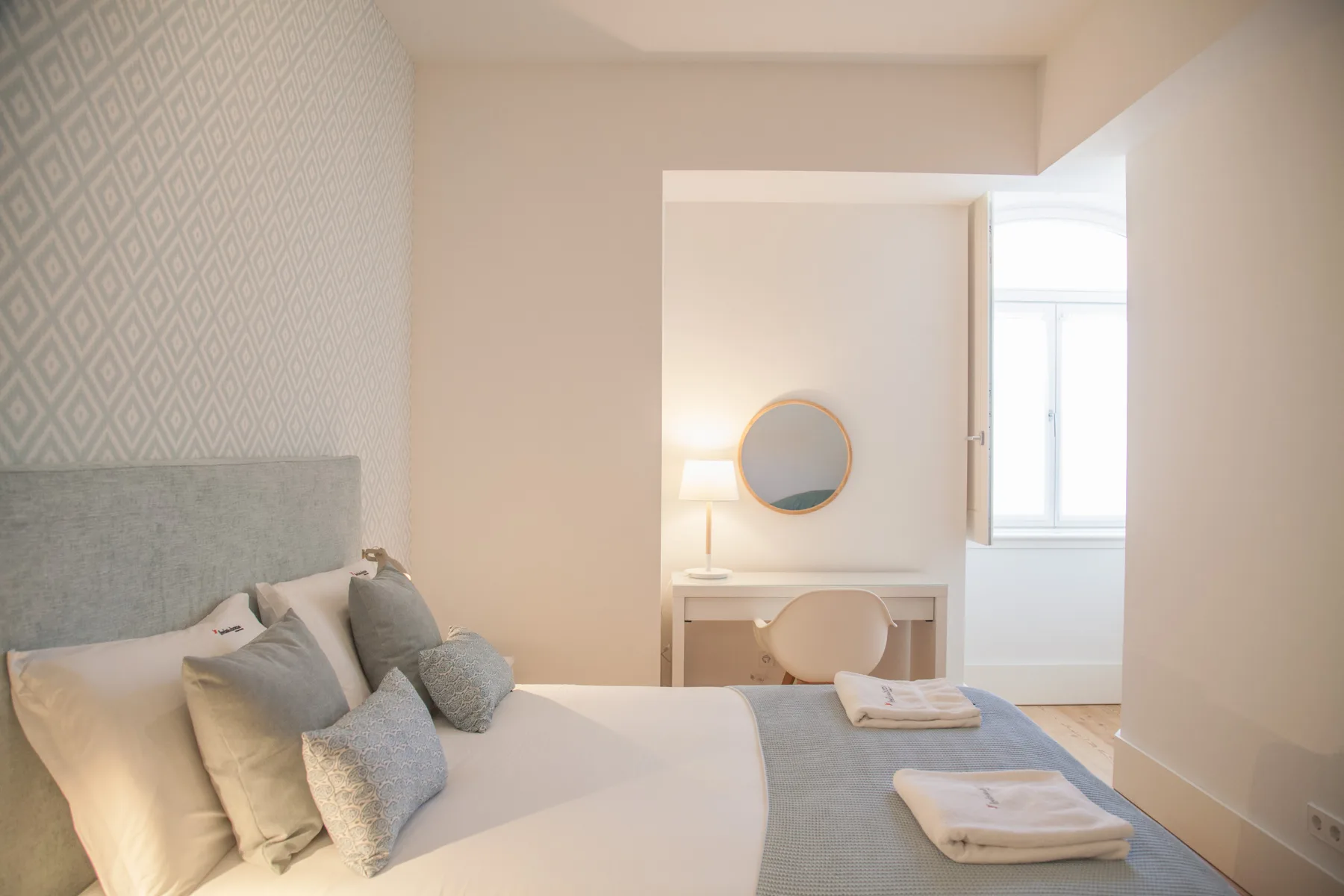 Un dormitorio con una cama, un escritorio y una ventana luminosa.
