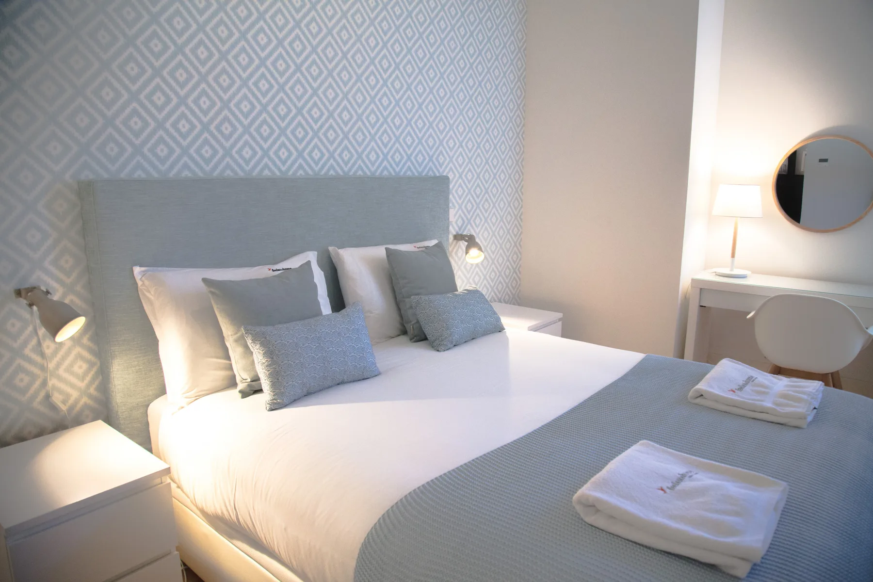 Dormitorio con una cama bien hecha y una pared estampada detrás.