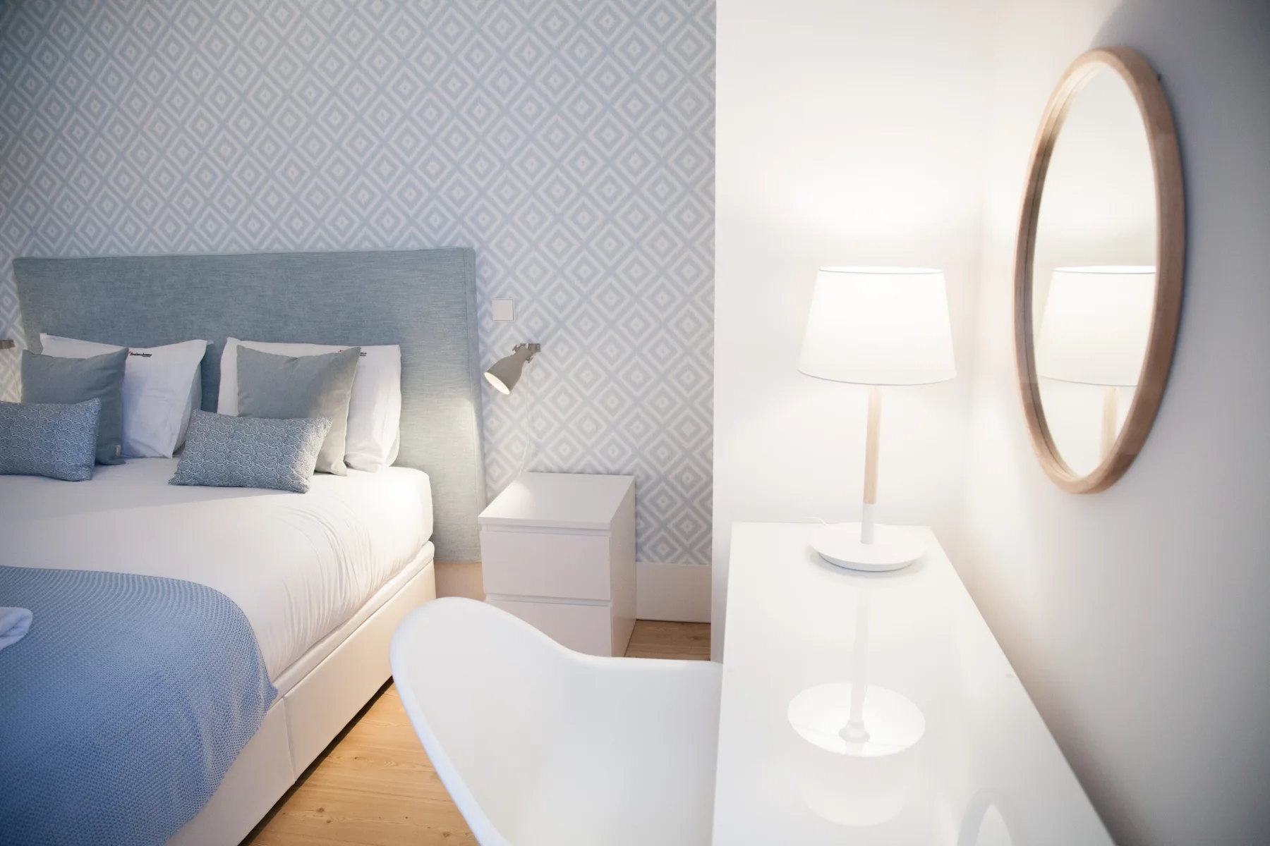 Un dormitorio con una cama bien tendida junto a un escritorio blanco y un espejo ovalado.