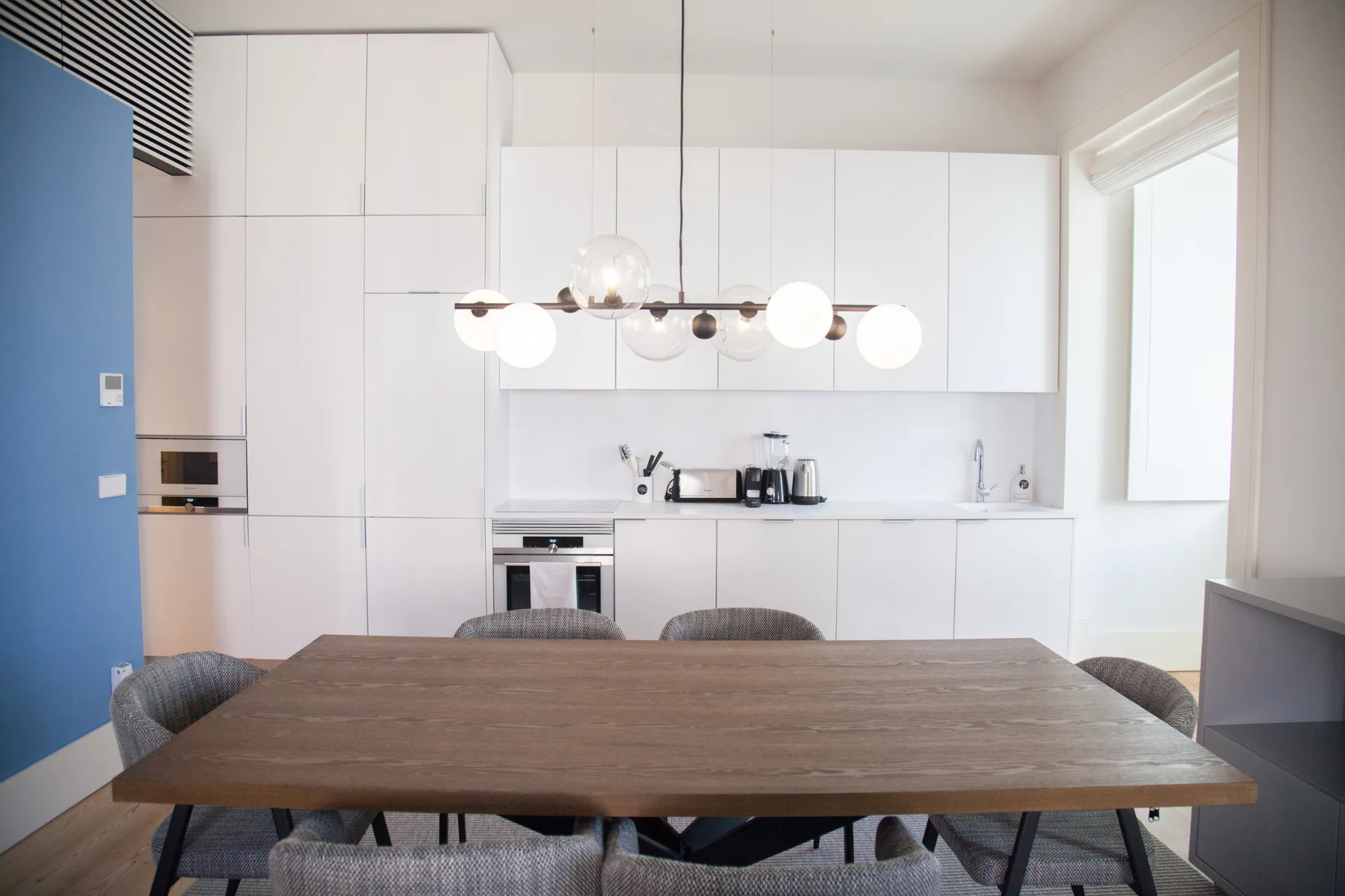 Comedor con una mesa de madera frente a una cocina blanca.