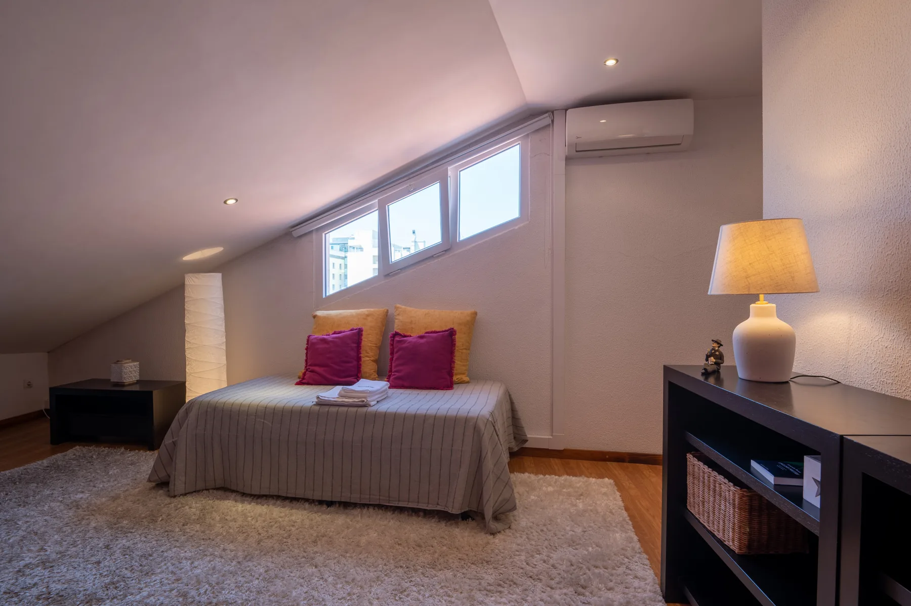 A bedroom with a bed beneath sloped ceilings and high windows.