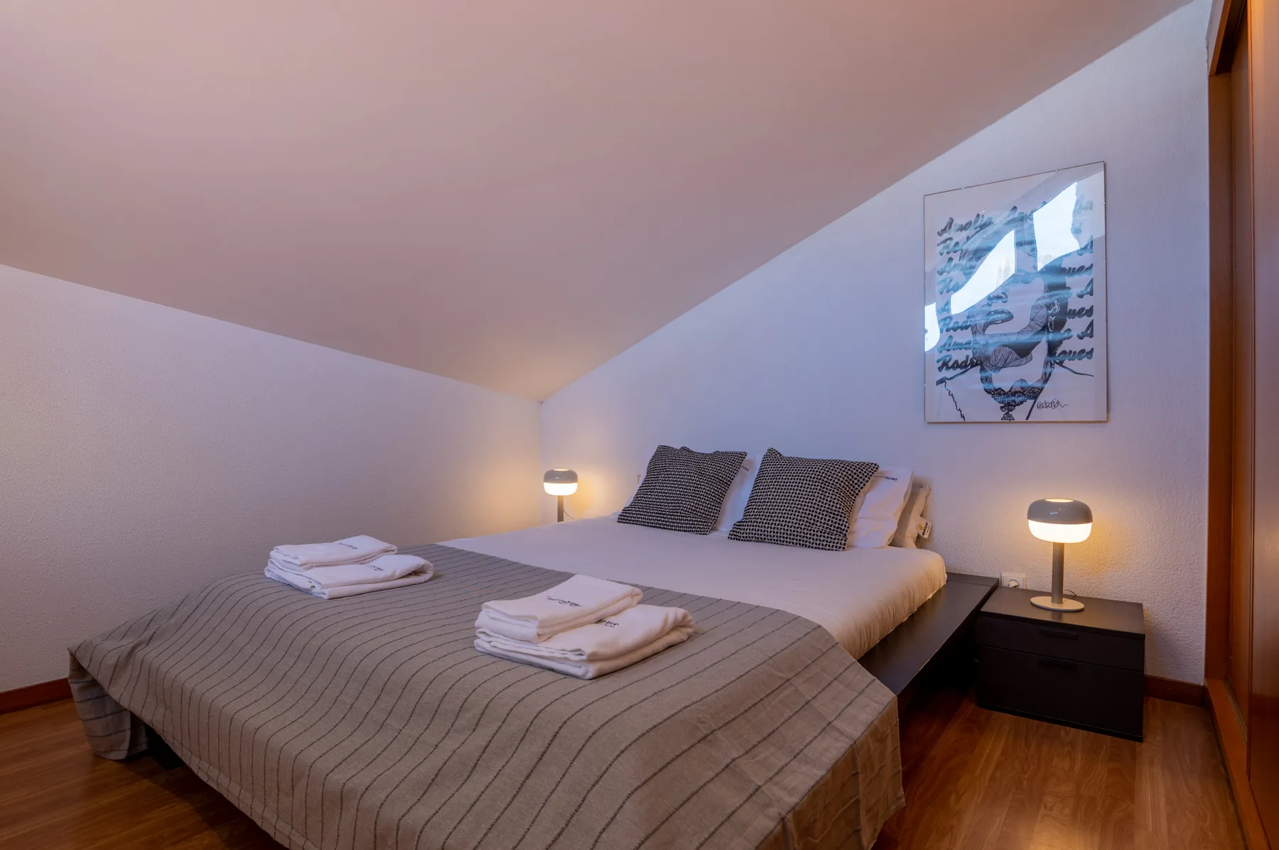 Un dormitorio con una cama hecha, toallas dobladas y lámparas de noche.