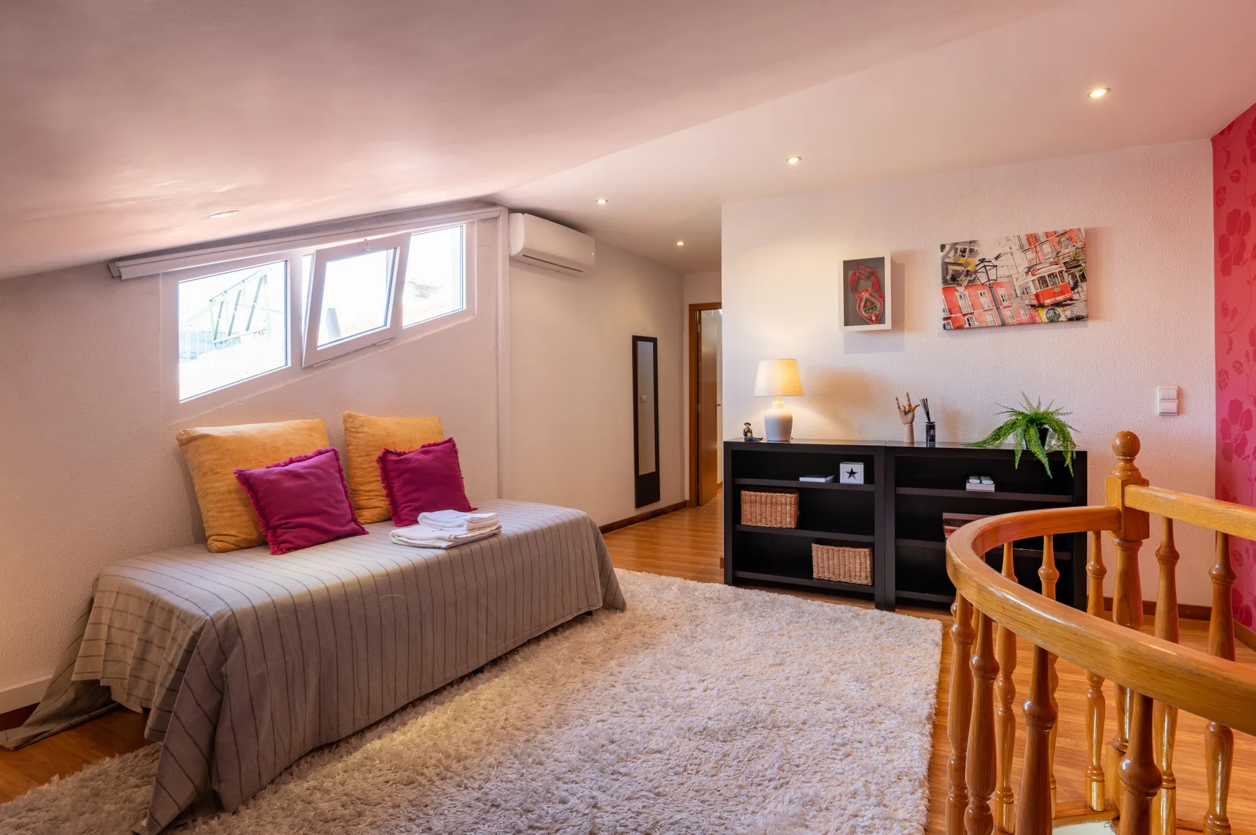 Un dormitorio con cama, mueble bajo de almacenaje y barandilla de madera.