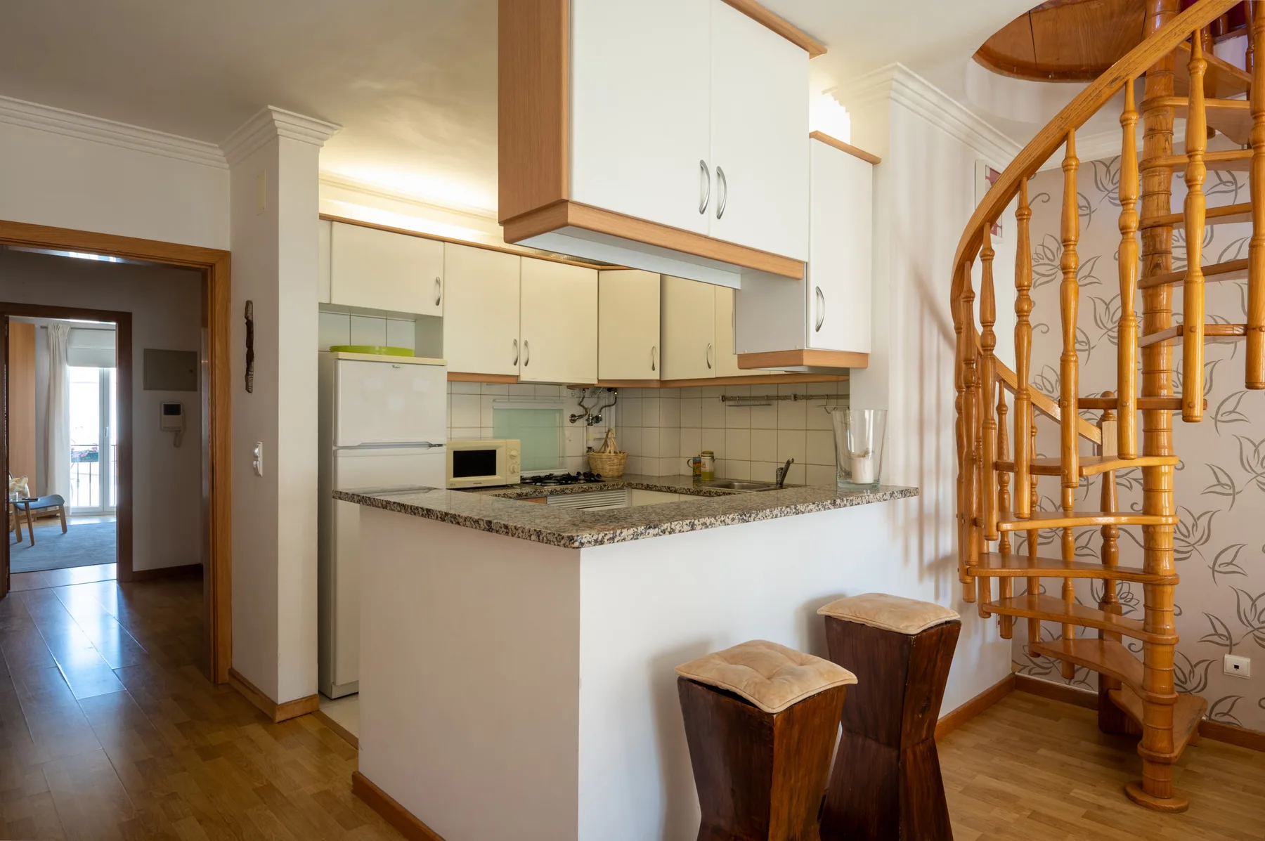 Una cocina compacta se abre a una barra junto a una escalera de caracol de madera.