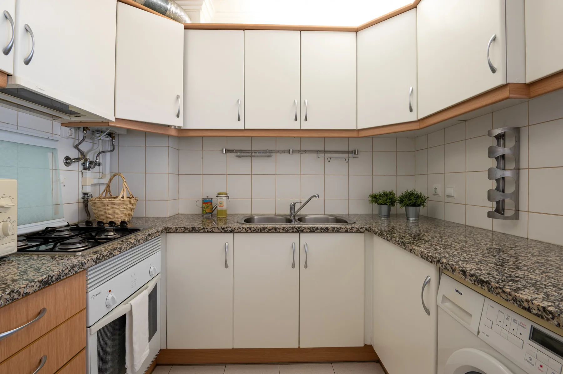 Una cocina compacta con armarios blancos, paredes de azulejos y encimeras oscuras.