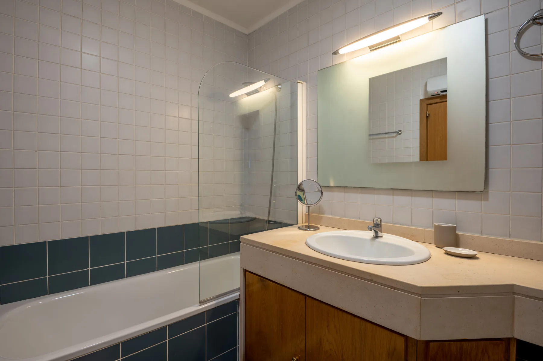 Un baño alicatado con bañera y lavabo bajo un espejo grande.
