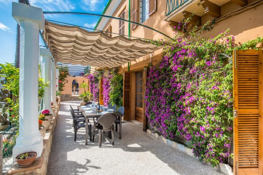 A sunlit outdoor patio with seating beneath a striped canopy and flowering vines.