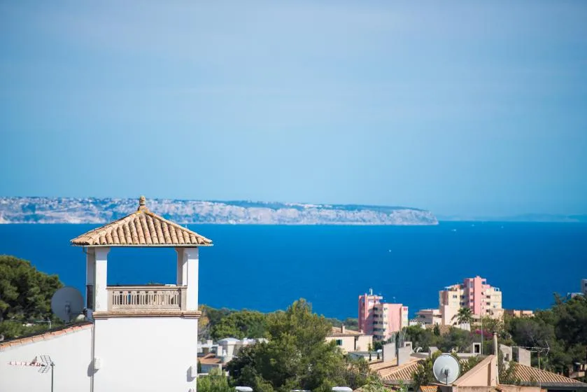 A coastal town overlooks blue water, with distant buildings along the shoreline.