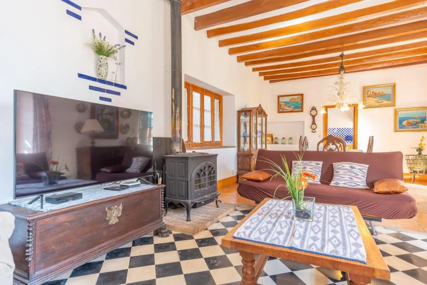 A living room with patterned tile flooring, exposed ceiling beams, and seating around a coffee table.