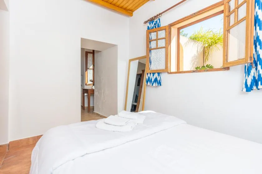 A bright bedroom with a neatly made bed and open wooden windows.
