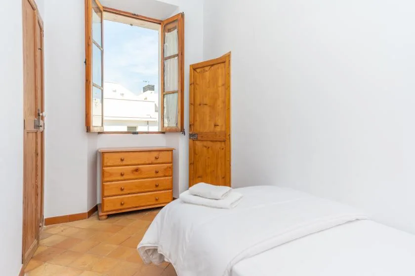 A bright bedroom with a white bed, wooden dresser, and open window.