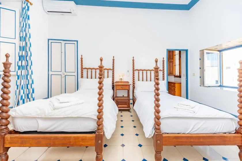 A bright bedroom with two beds and a small wooden bedside table.