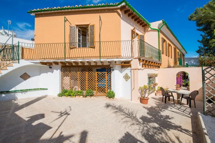 A peach-colored two-story house faces a paved courtyard with outdoor seating.
