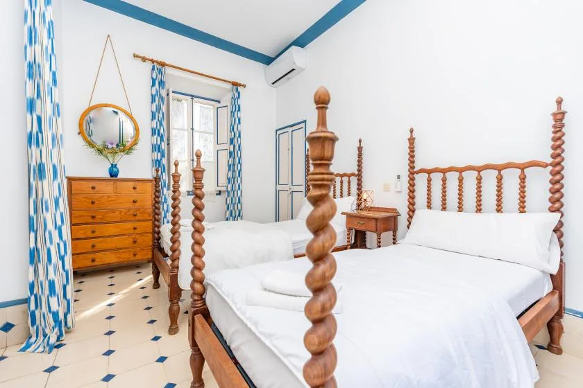 A bright bedroom with two wooden beds, white bedding, and blue accents.