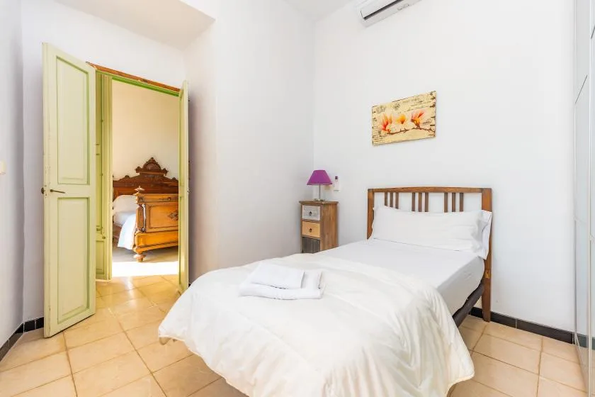 A bright bedroom with a wooden bed, white bedding, and an open doorway.