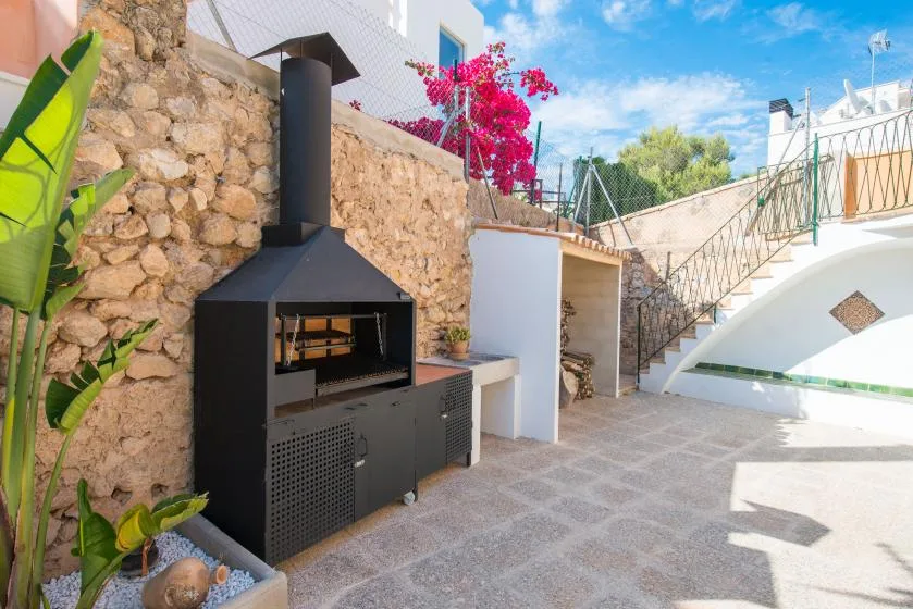 A paved outdoor patio features a built-in barbecue beside a stone wall and staircase.