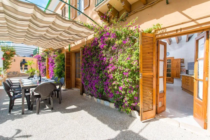 A sunny courtyard dining area with outdoor seating, flowering vines, and open doors.