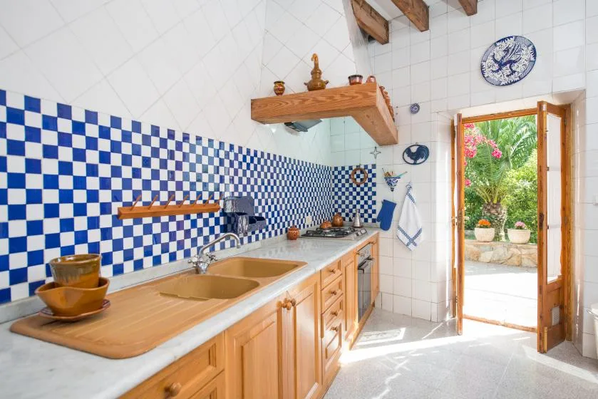 A tiled kitchen with a long countertop and an open doorway to a garden.