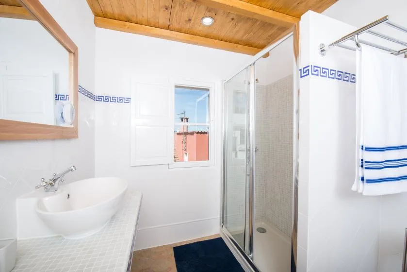 A bright bathroom with a sink, glass shower, and wooden ceiling.