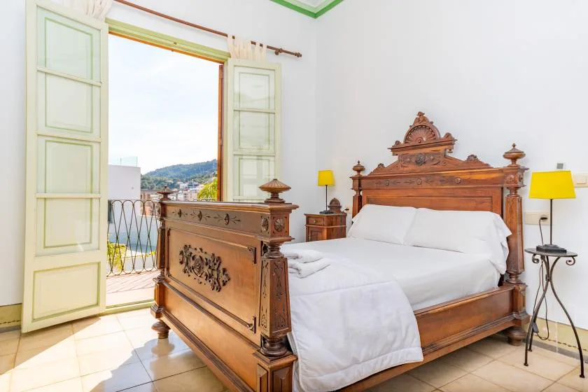 A bedroom with an ornate wooden bed and open doors to a balcony.