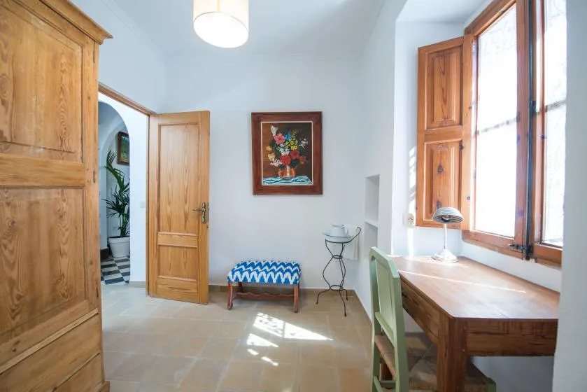 A bright room with a wooden desk beside tall windows and an open doorway.