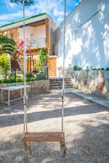 A gravel courtyard with a wooden swing in front of a house.