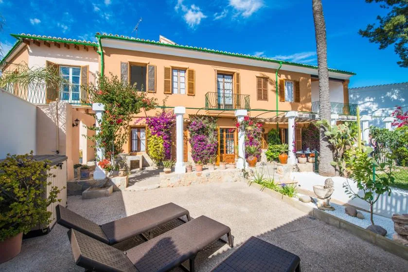 A peach-colored house faces a sunny patio with lounge seating and flowering vines.