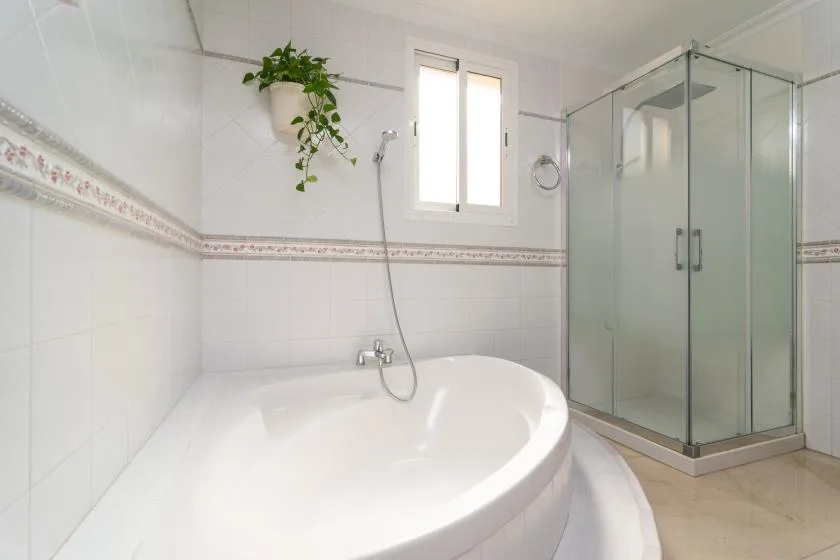 A tiled bathroom features a curved bathtub beside a glass shower.