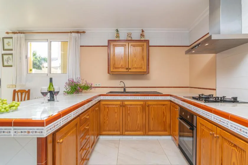 A bright kitchen with wooden cabinets, tiled counters, and a window.