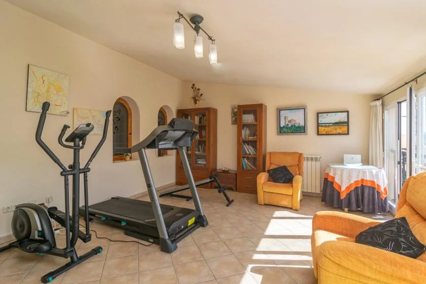 A living room with exercise equipment, orange seating, and large windows.