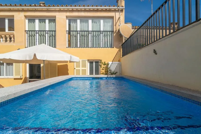 An outdoor swimming pool beside a yellow building and a shaded patio.