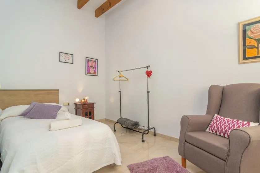 A bedroom with a bed and an armchair beside a clothes rack.