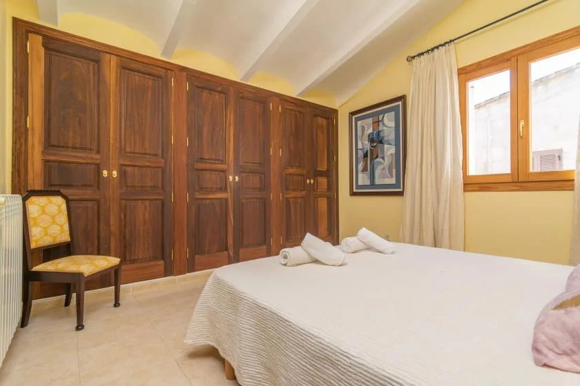 A bedroom with a large bed, dark wooden wardrobes, and a window.