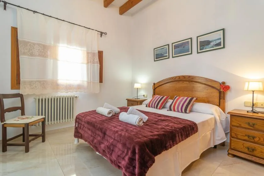 A bedroom with a wooden bed, striped pillows, and a window with sheer curtains.