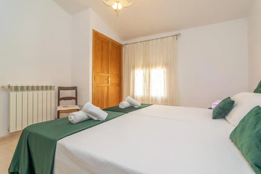 A bedroom with a large bed, green bedding, and a curtained window.