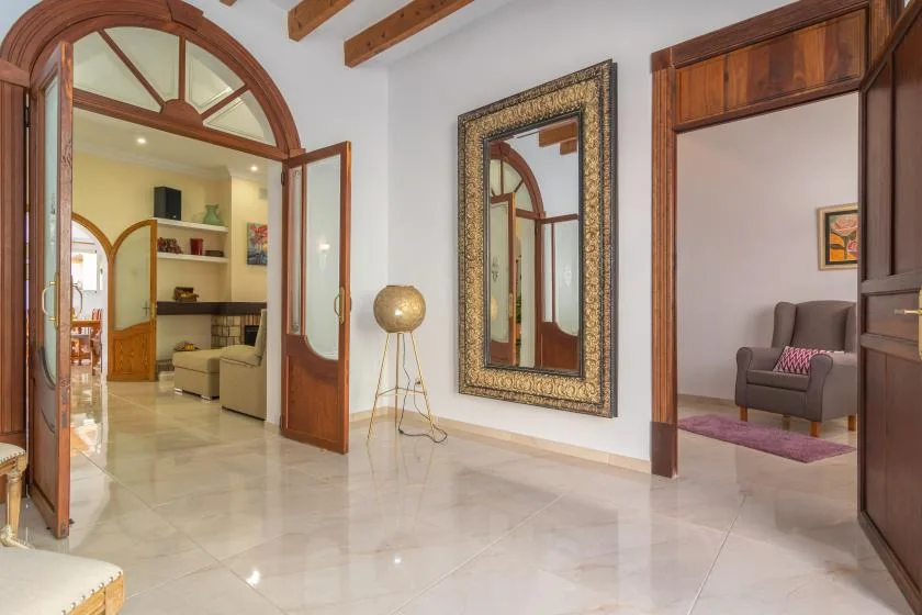 A bright interior hallway with wooden doorways, a wall mirror, and polished tile flooring.