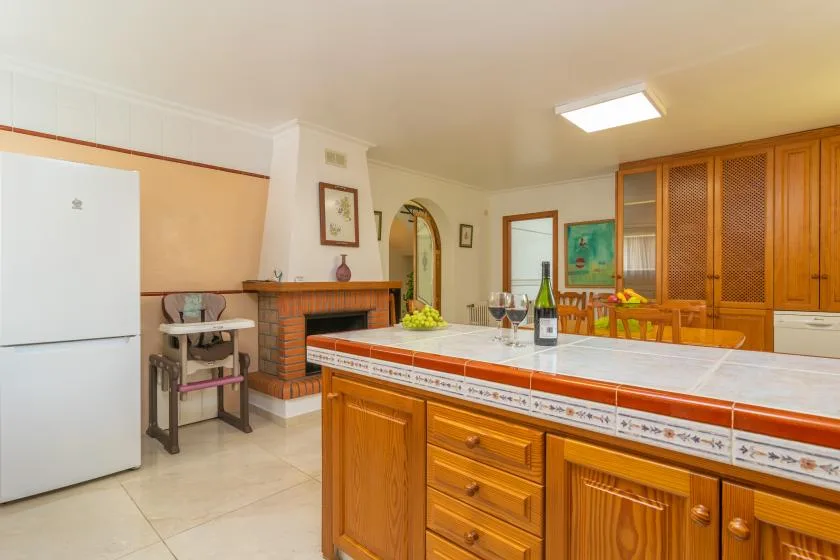 A kitchen with a long tiled counter, wooden cabinets, and a refrigerator.