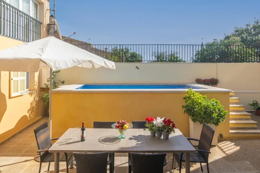 An outdoor dining area beside a swimming pool, with a table under a patio umbrella.