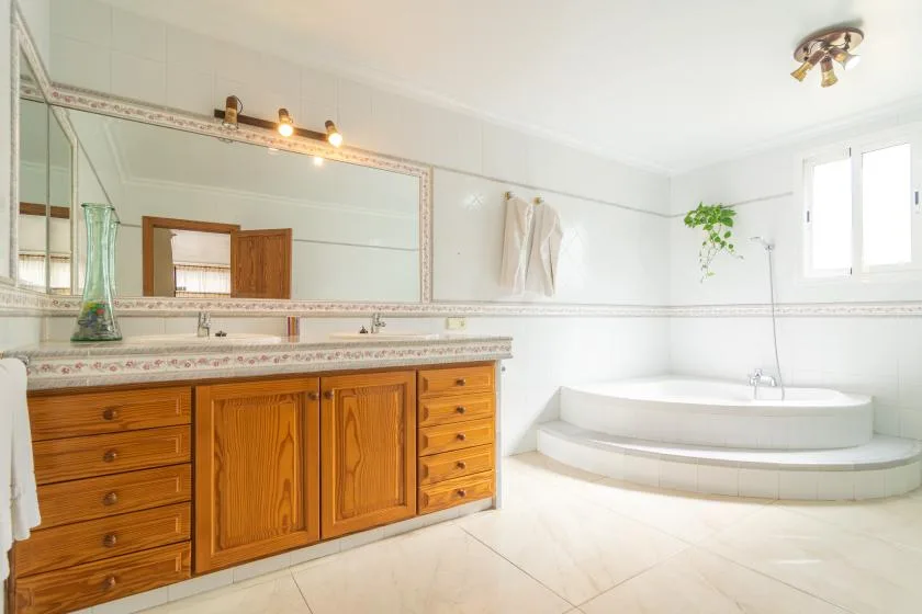 A bright bathroom has a wooden vanity, a large mirror, and a raised bathtub.